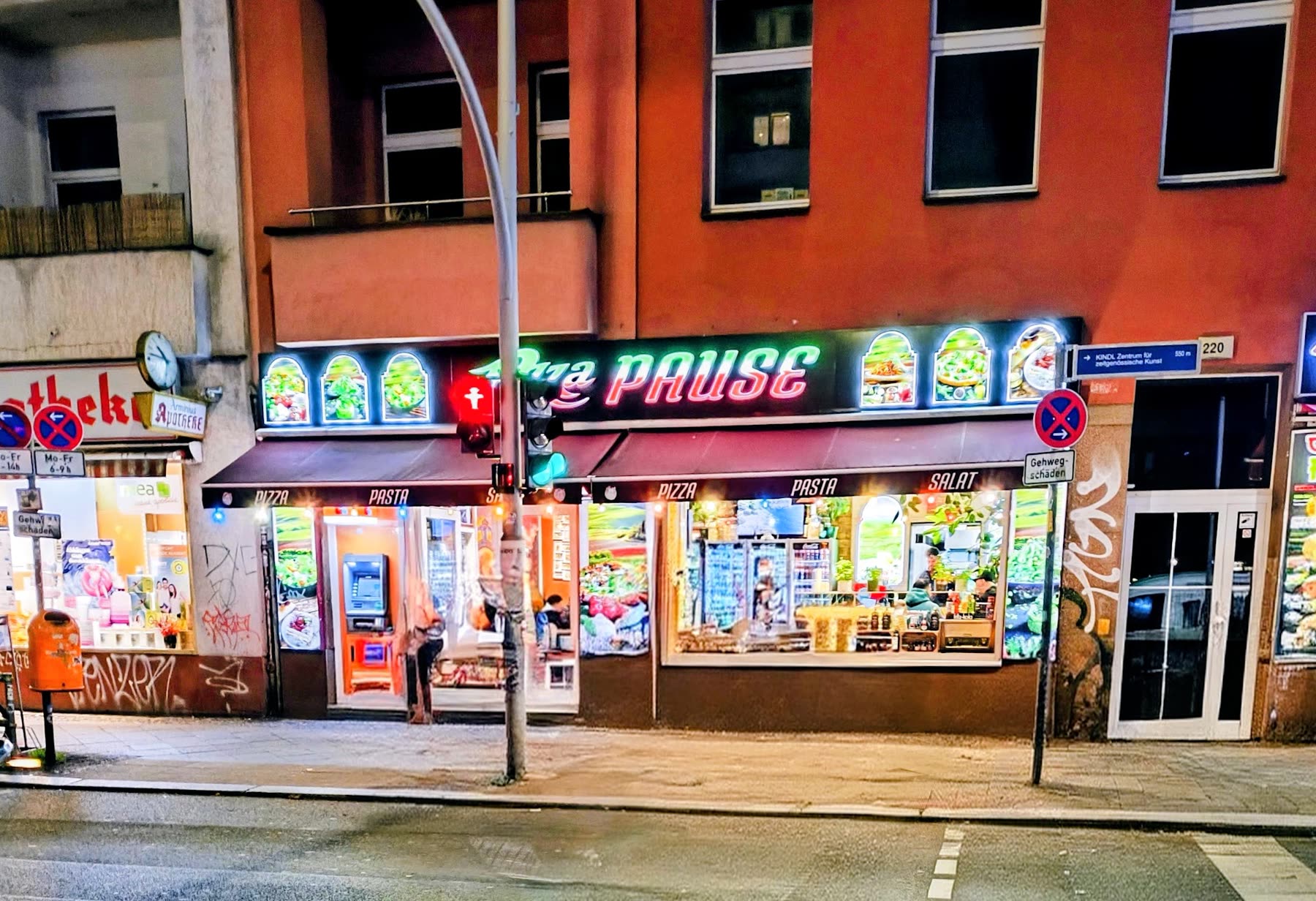 Fassade von Pizza Pause an der Hermannstraße 220 bei Nacht, mit leuchtendem Neon-Banner und Rundbogen-Arkaden